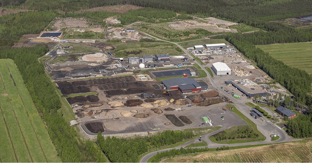 Näkymä omakotitalon pihatielle, vasemmassa laidassa valkoinen jätekatos, jonka räystäässä roikkuu kukka-amppeli.